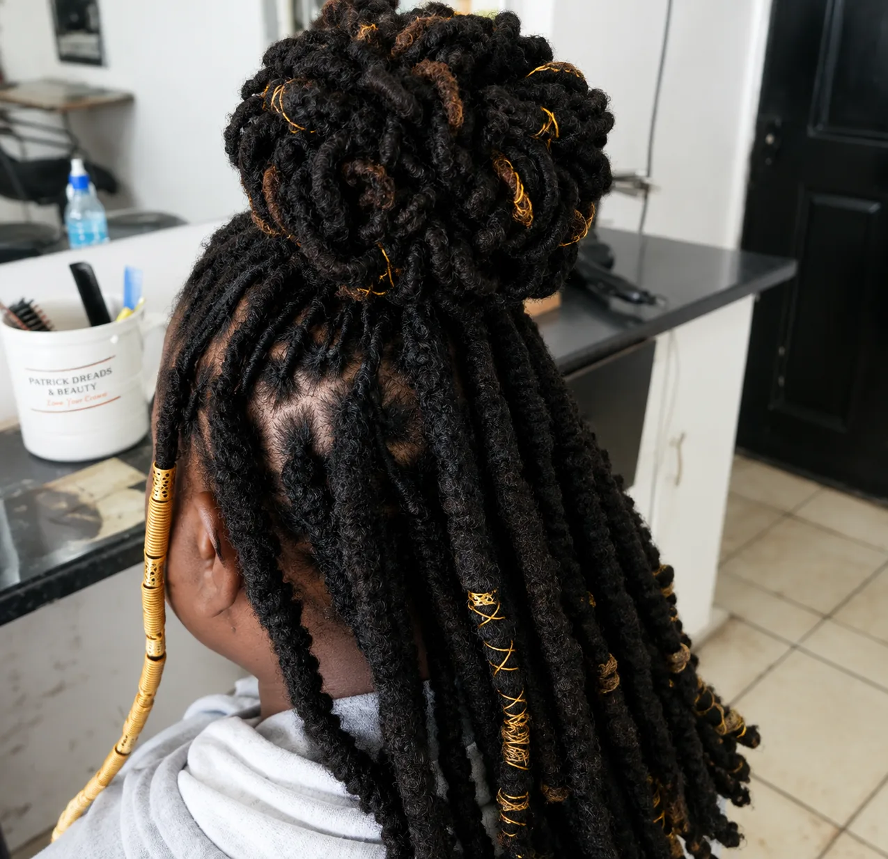 Long locs dressed with gold cuffs and thread, gathered into a half-up bun